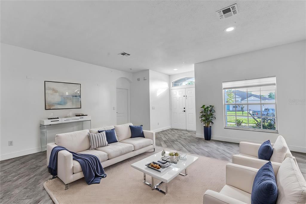 A bright living room features white sofas, a coffee table, and gray wood-look flooring — 2031 WINTERMERE POINTE DRIVE, WINTER GARDEN, FL