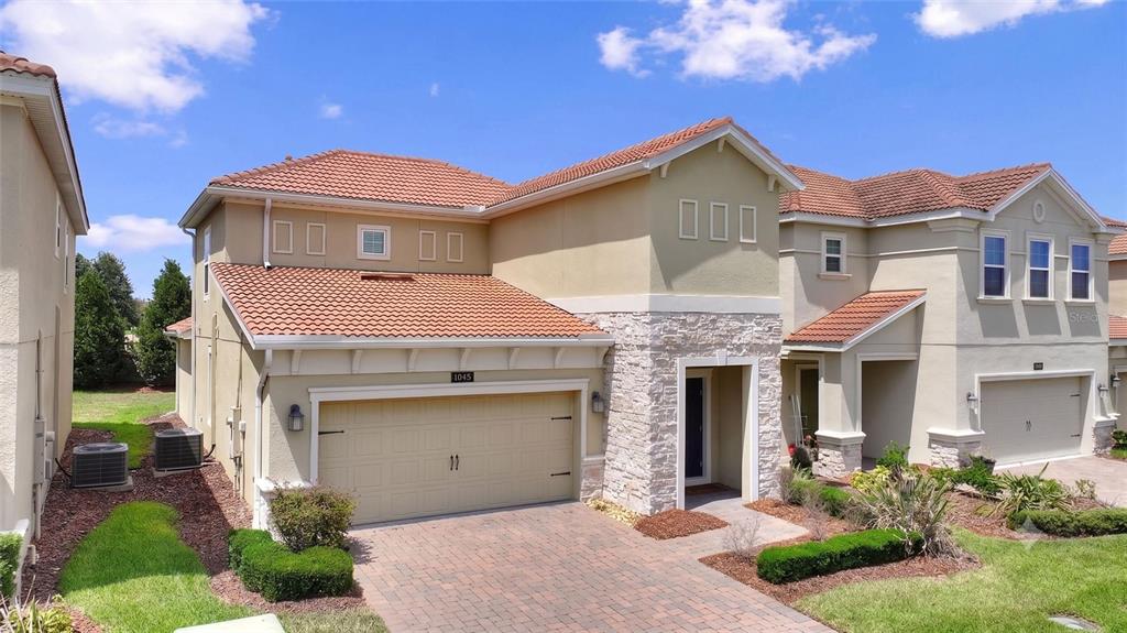 A two-story house with a tan stucco exterior, stone accents, and a tiled roof — 1045 BLACKWOLF RUN RD, DAVENPORT, FL