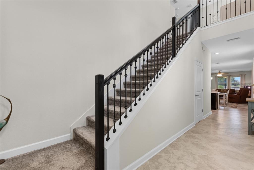 A carpeted staircase with black metal balusters and a dark wood handrail leads upstairs — 1045 BLACKWOLF RUN RD, DAVENPORT, FL