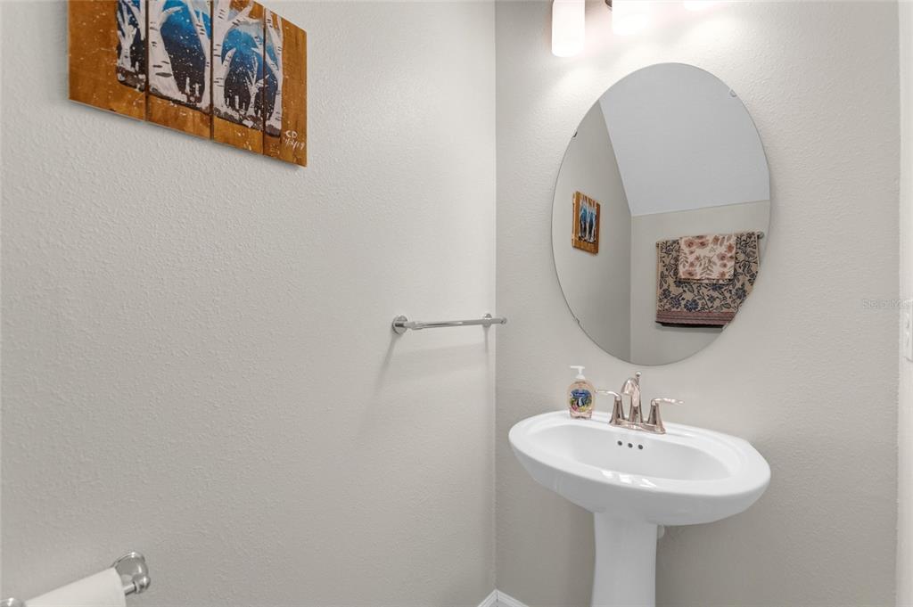 A powder room features a white pedestal sink, an oval mirror, and wall-mounted artwork — 1045 BLACKWOLF RUN RD, DAVENPORT, FL