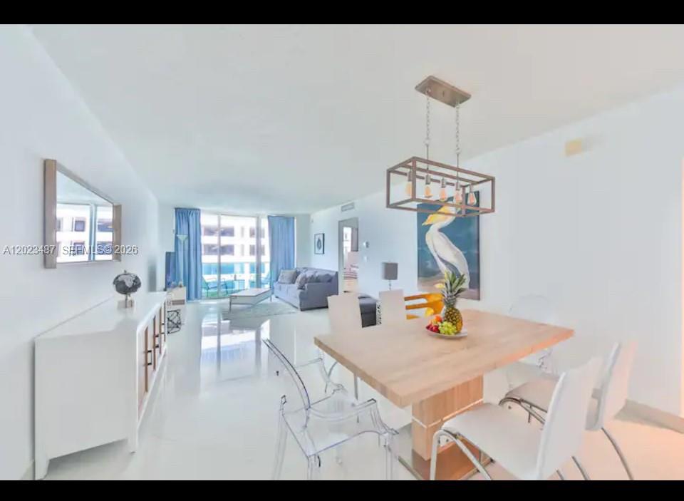 A bright dining area with a wooden table and clear chairs leads into a living room — 4001 S Ocean Dr # 7L, Hollywood FL 33019, HOLLYWOOD, FL