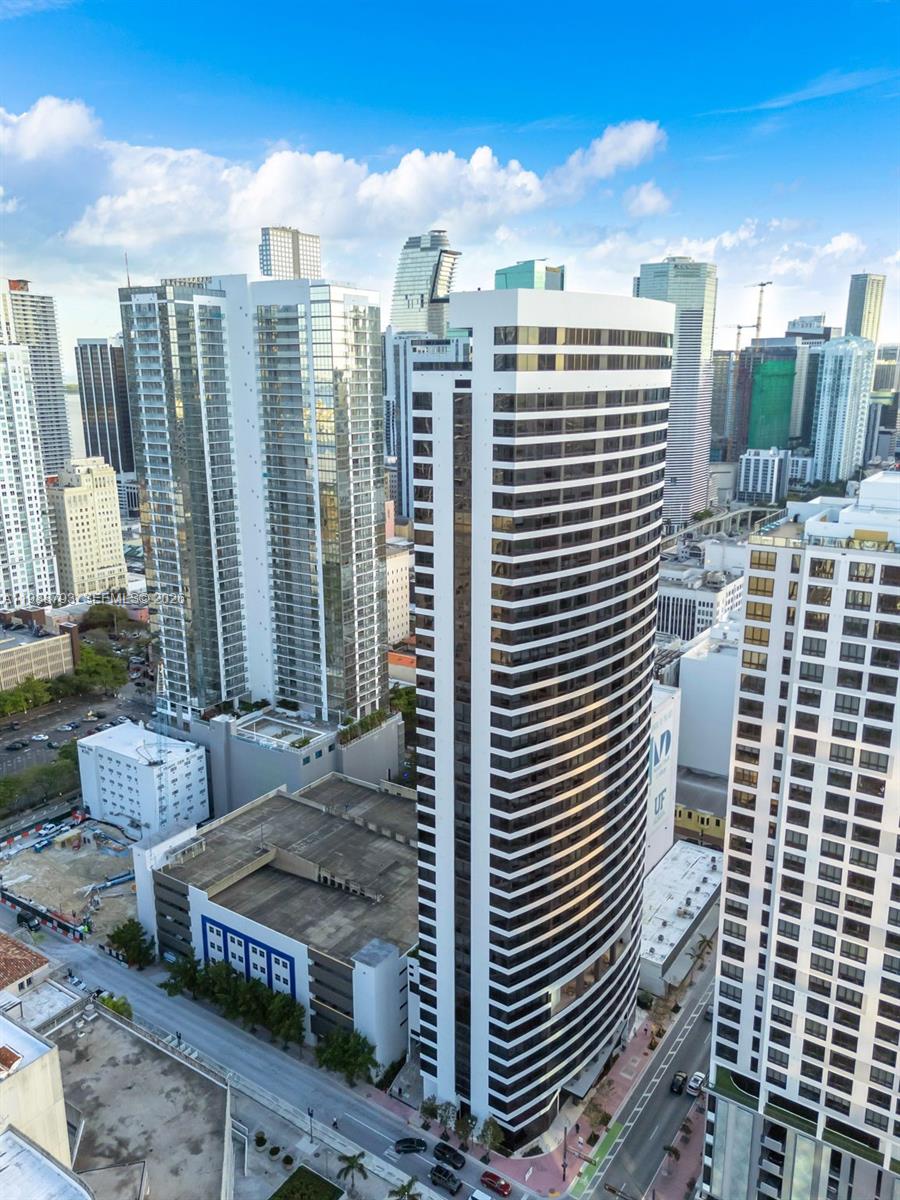 An aerial view shows a tall, modern office building surrounded by other skyscrapers in Miami — 225 N Miami # 1705, Miami FL 33131, MIAMI, FL