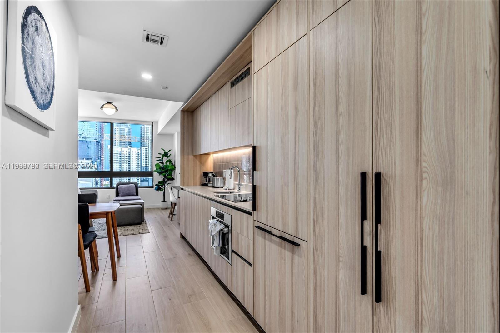 A modern kitchen features light wood cabinetry, integrated appliances, and a view of city buildings — 225 N Miami # 1705, Miami FL 33131, MIAMI, FL
