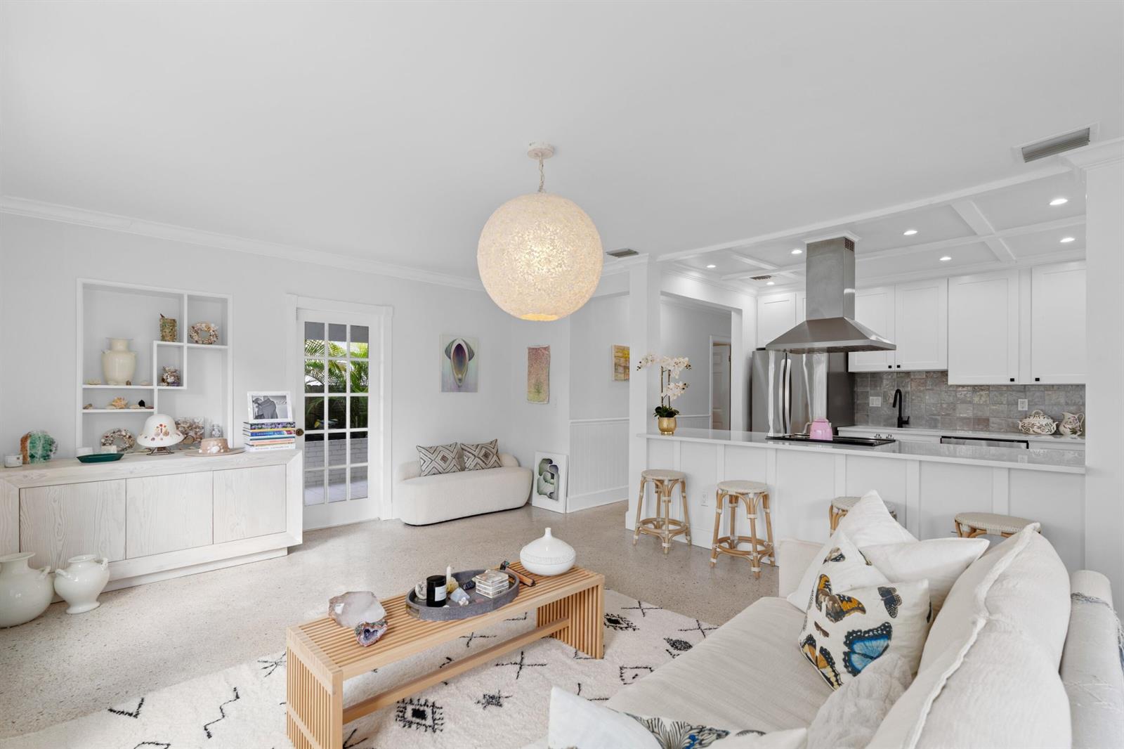A bright, open-concept living room and kitchen featuring white cabinetry, a large pendant light, and terrazzo flooring — 143 Greymon Drive, West Palm Beach FL 33405, WEST PALM BEACH, FL