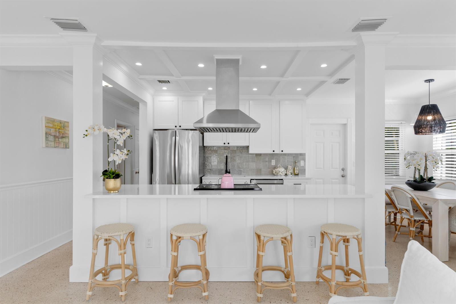 A white kitchen features a breakfast bar with four rattan stools and stainless steel appliances — 143 Greymon Drive, West Palm Beach FL 33405, WEST PALM BEACH, FL