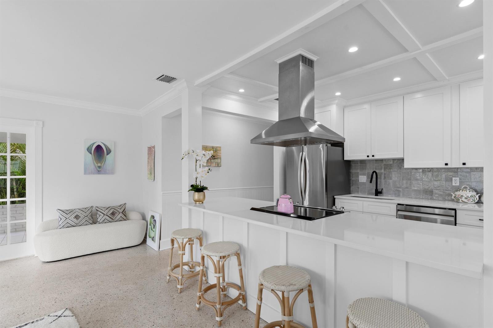 A white kitchen features a breakfast bar with stools, stainless steel appliances, and tile backsplash — 143 Greymon Drive, West Palm Beach FL 33405, WEST PALM BEACH, FL