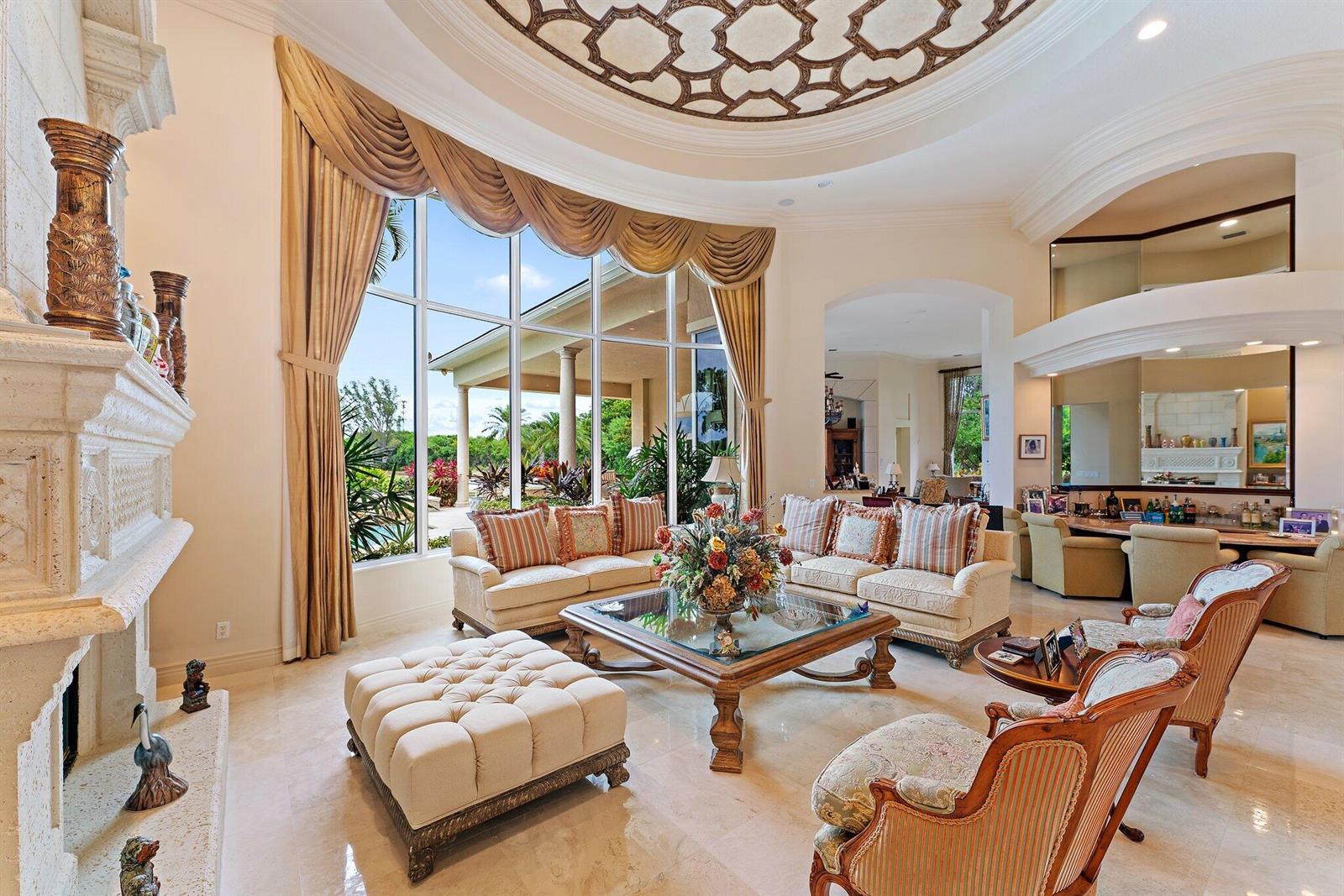 A spacious living room features a stone fireplace, floor-to-ceiling windows, and a decorative ceiling — 12049 SE Intracoastal Terrace, Jupiter FL 33469, JUPITER, FL