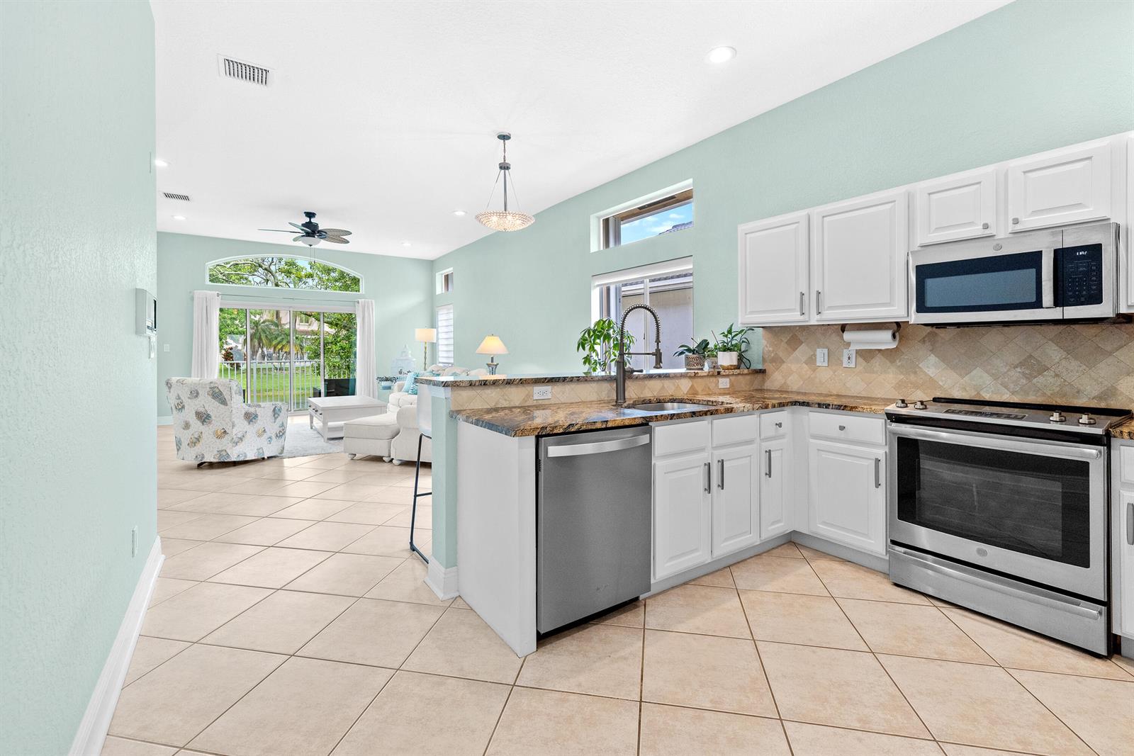 A kitchen with white cabinets and stainless steel appliances overlooks an open-concept living area — 6513 Sandpiper Drive, Coconut Creek FL 33073, COCONUT CREEK, FL