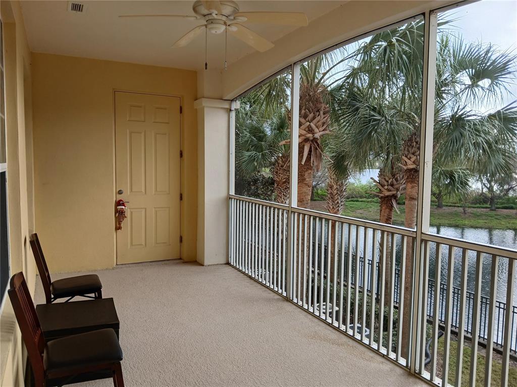 A screened-in balcony features a ceiling fan, beige carpet, two chairs, and a water view — 3368 ROBERT TRENT JONES DRIVE UNIT 20608, ORLANDO, FL