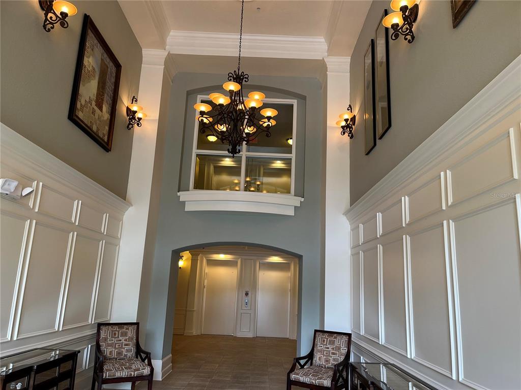 A high-ceilinged lobby features white wainscoting, a large chandelier, and two elevator doors — 3368 ROBERT TRENT JONES DRIVE UNIT 20608, ORLANDO, FL
