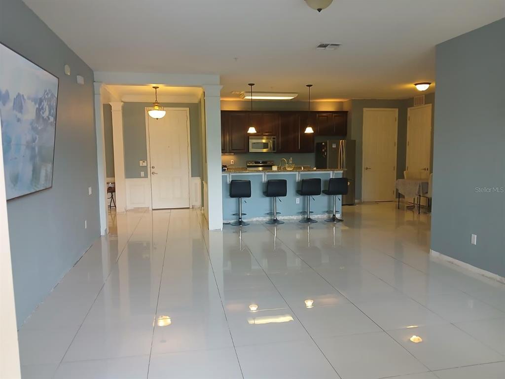A kitchen with dark cabinets and a breakfast bar overlooks a large, tiled living area — 3368 ROBERT TRENT JONES DRIVE UNIT 20608, ORLANDO, FL