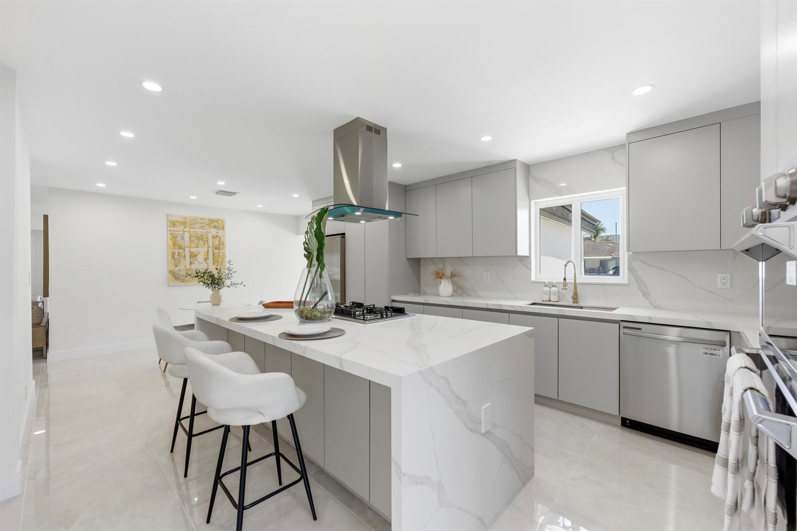 A modern kitchen features a marble waterfall island, gray cabinetry, and stainless steel appliances — 2280 SE 10th Court, Pompano Beach FL 33062, POMPANO BEACH, FL