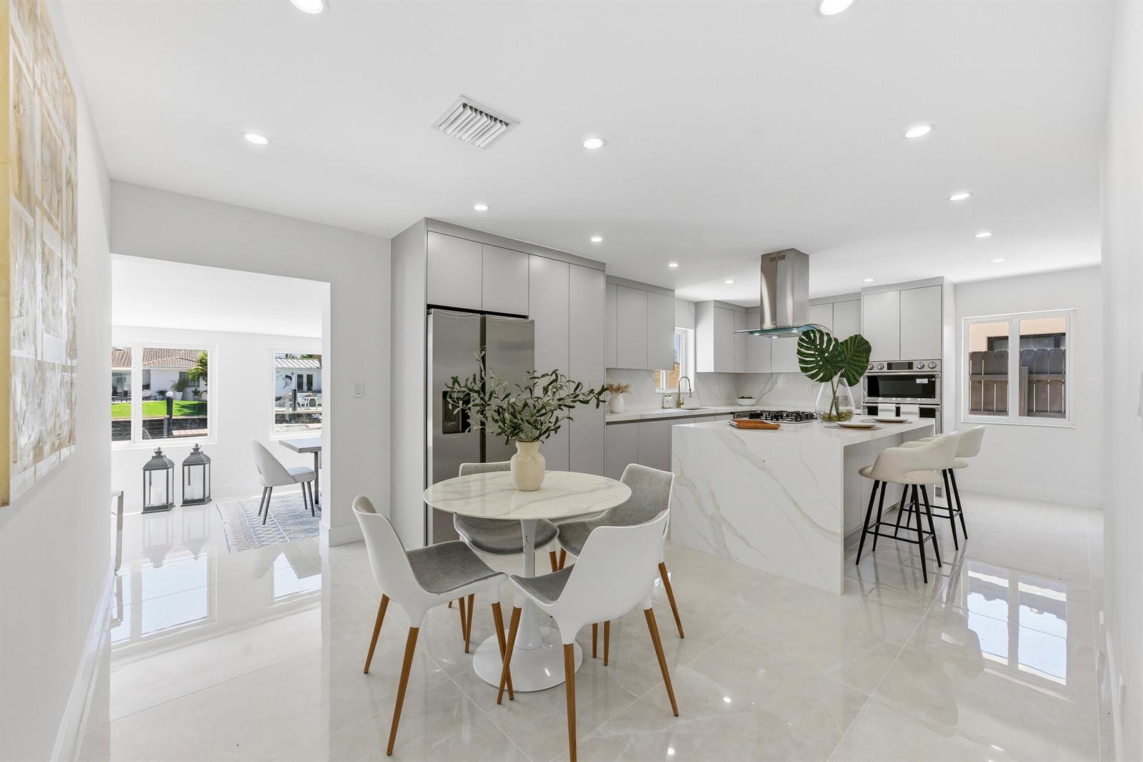 A modern kitchen features a marble island, white cabinetry, and an adjacent dining area — 2280 SE 10th Court, Pompano Beach FL 33062, POMPANO BEACH, FL