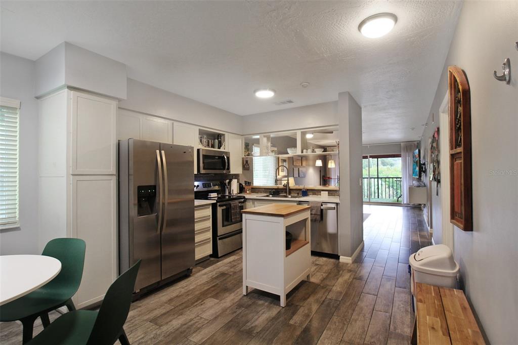 A kitchen with stainless steel appliances, white cabinets, a wooden island, and wood-look flooring — 2124 N TAMIAMI TRAIL UNIT 101, SARASOTA, FL