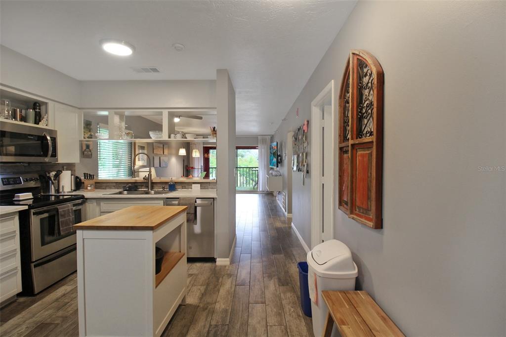 A kitchen with white cabinets and a wood-topped island opens to a hallway with wood-look flooring — 2124 N TAMIAMI TRAIL UNIT 101, SARASOTA, FL