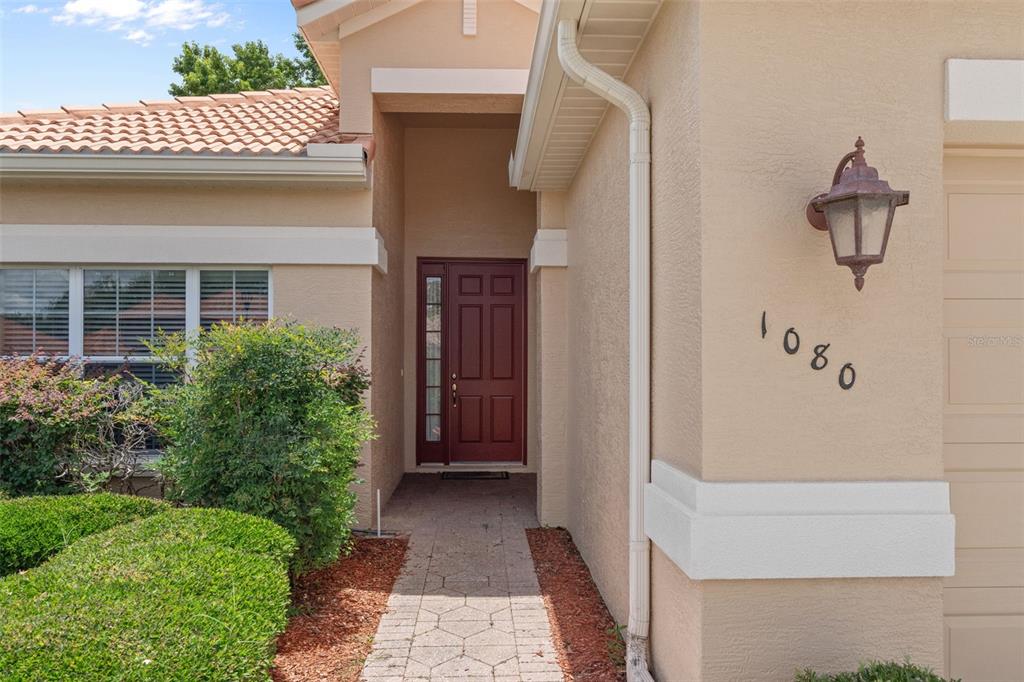 The exterior of a tan house features a red front door and a paved walkway — 1080 W SKYVIEW CROSSING DRIVE, HERNANDO, FL
