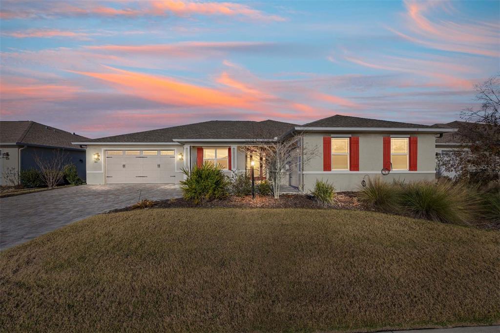 A single-story suburban house with a two-car garage and red shutters at sunset — 8111 SW 95TH COURT, OCALA, FL
