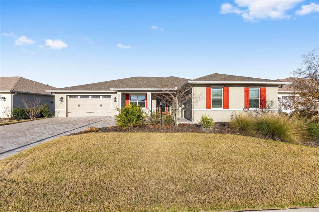 A single-story suburban house with a tan stucco exterior, red shutters, and a paved driveway — 8111 SW 95TH COURT, OCALA, FL