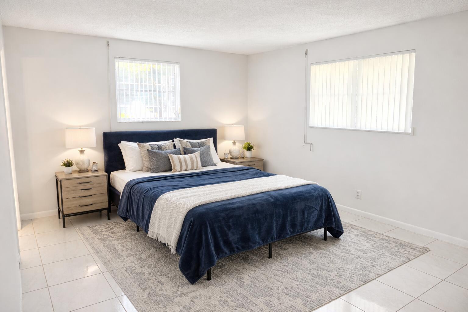 A bedroom features a blue upholstered bed, two nightstands, and a gray area rug — 2687 Garden Drive N # 212, FL 33461, FL