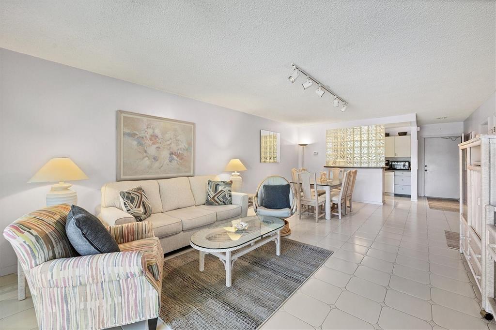 A living room with a beige sofa, patterned armchair, glass coffee table, and dining area — 500 S WASHINGTON DRIVE UNIT 5B, SARASOTA, FL