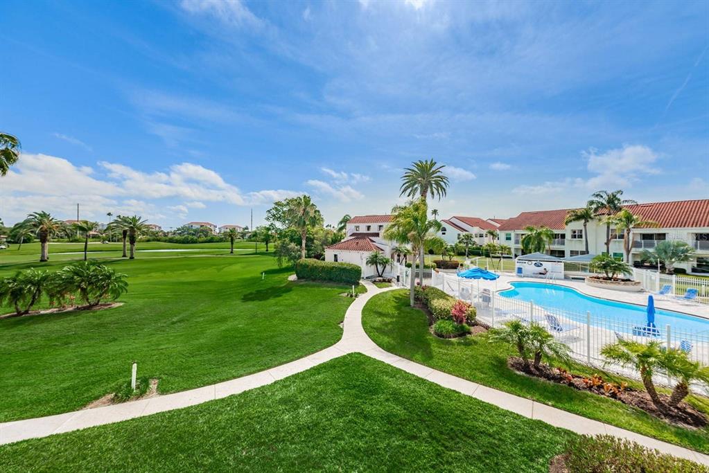 An outdoor view of a swimming pool, a grassy lawn, and residential buildings under a sky — 6059 BAHIA DEL MAR BOULEVARD UNIT 241, ST PETERSBURG, FL