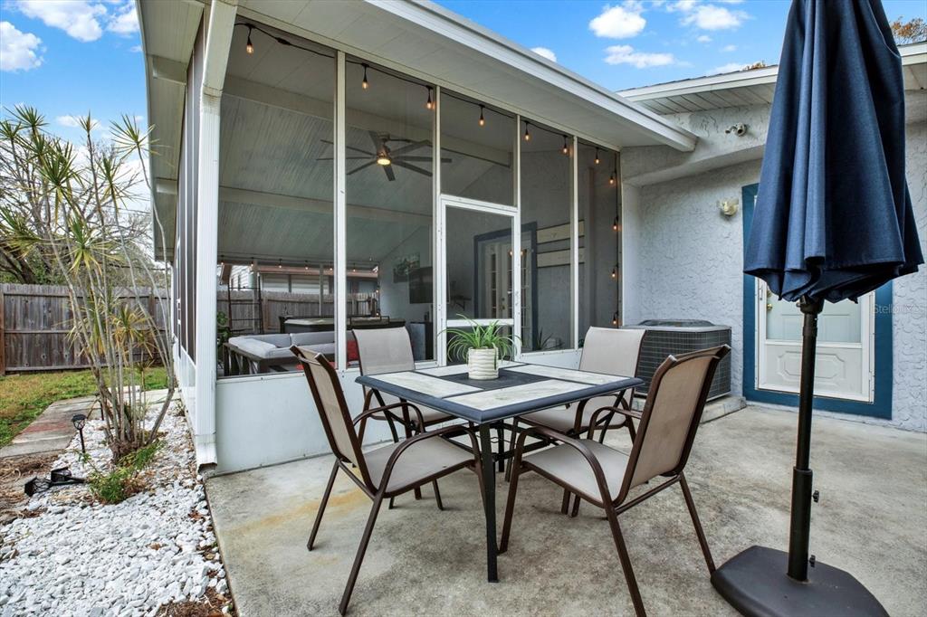 A patio with a dining set and umbrella sits outside a screened-in porch — 4432 73RD AVENUE N, PINELLAS PARK, FL