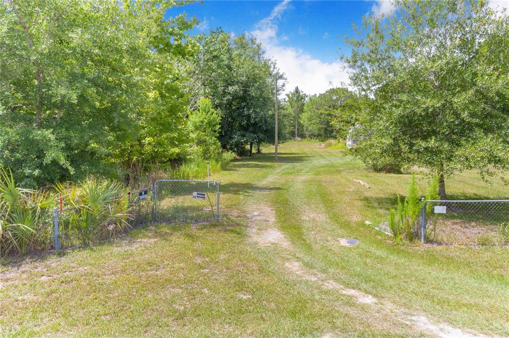 A gated entrance leads to a grassy driveway on a wooded residential lot — 6873 WILBAR LANE, HAINES CITY, FL