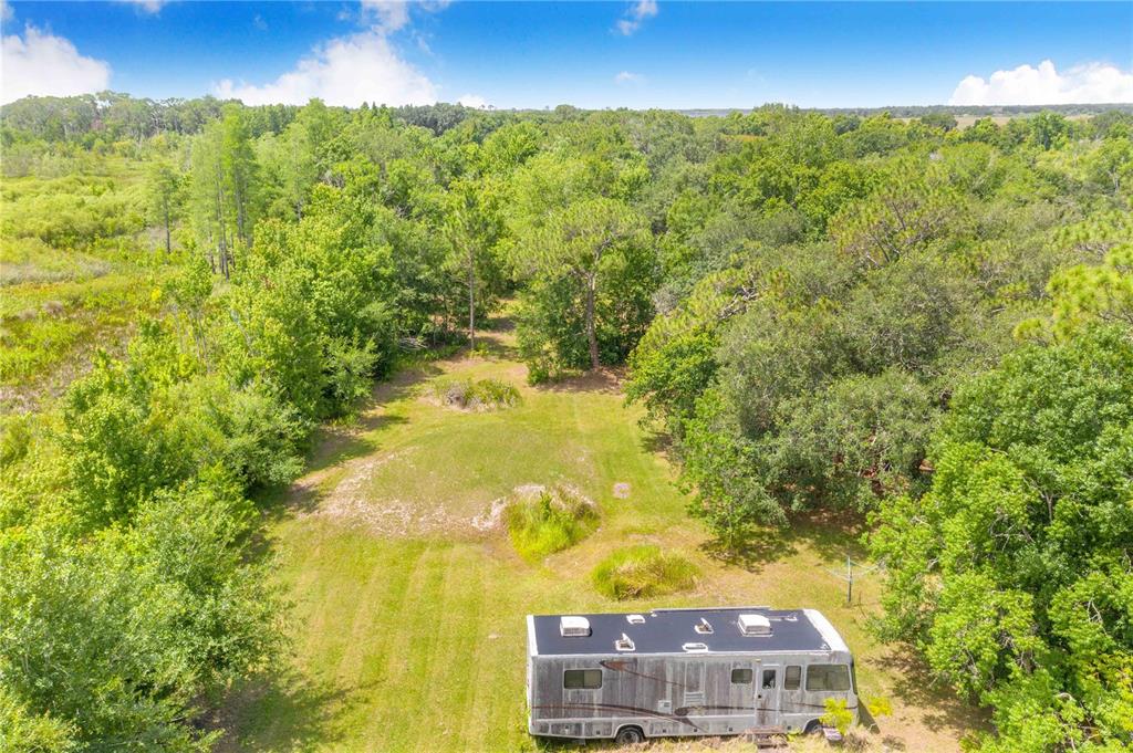 An aerial view shows a recreational vehicle parked on a grassy lot surrounded by trees — 6873 WILBAR LANE, HAINES CITY, FL