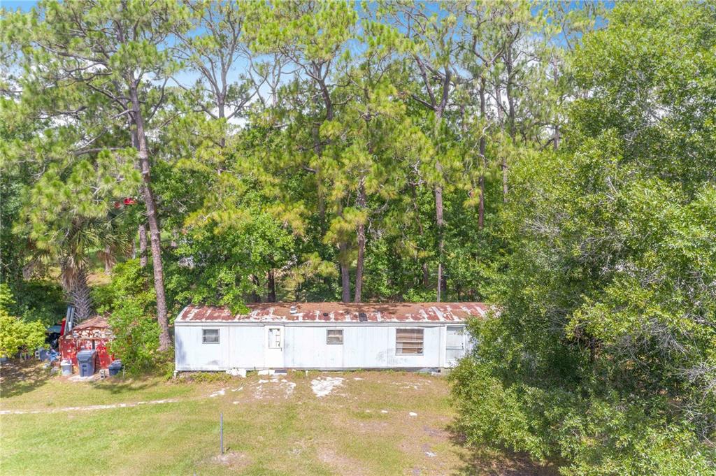 An aerial view of a weathered mobile home situated in a wooded, grassy lot — 6873 WILBAR LANE, HAINES CITY, FL