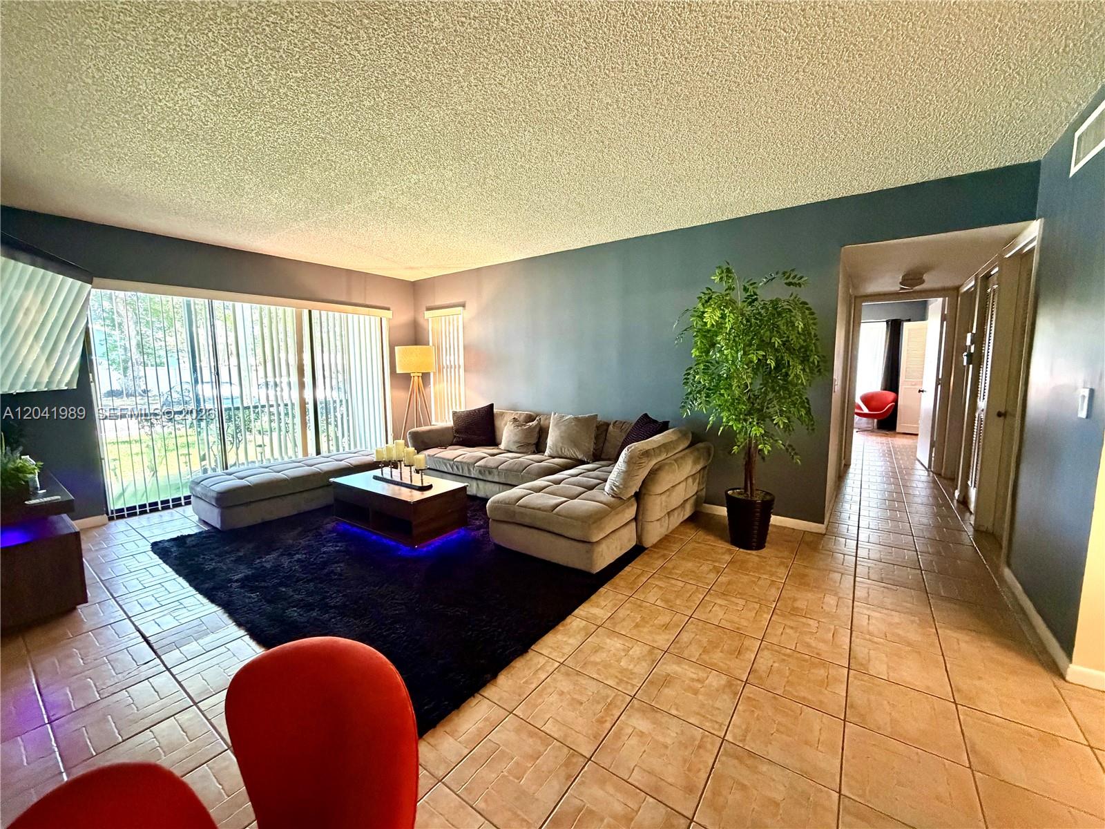 A living room features a large sectional sofa, a dark rug, and tile flooring — 1119 Green Pine Blvd # A1, West Palm Beach FL 33409, WEST PALM BEACH, FL