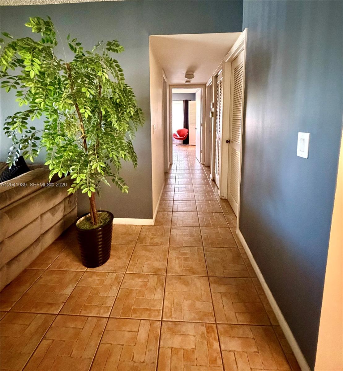 A hallway with tiled floors leads past louvered closet doors toward a distant room — 1119 Green Pine Blvd # A1, West Palm Beach FL 33409, WEST PALM BEACH, FL