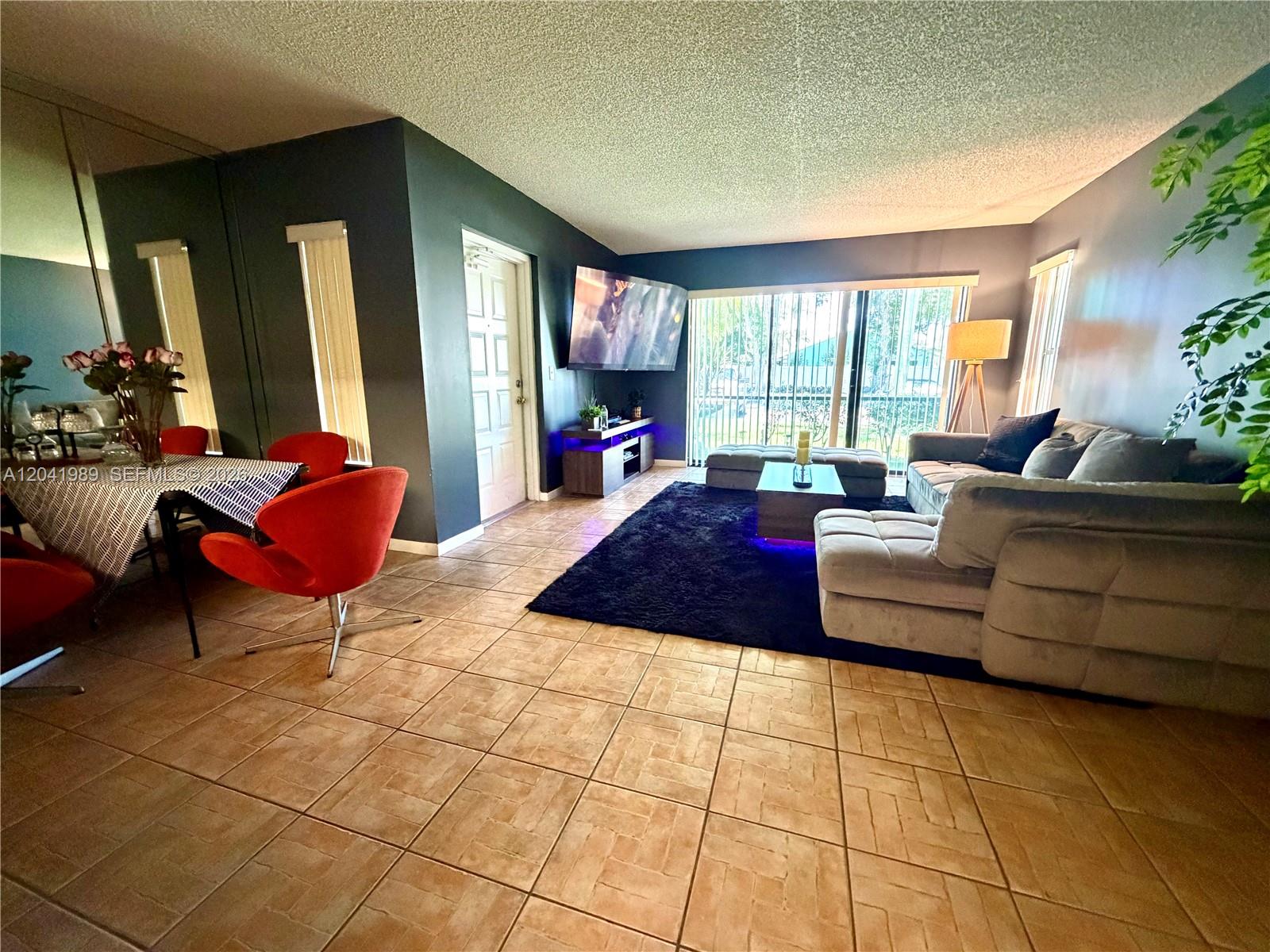 A living and dining area features tile flooring, dark walls, a sectional sofa, and red chairs — 1119 Green Pine Blvd # A1, West Palm Beach FL 33409, WEST PALM BEACH, FL