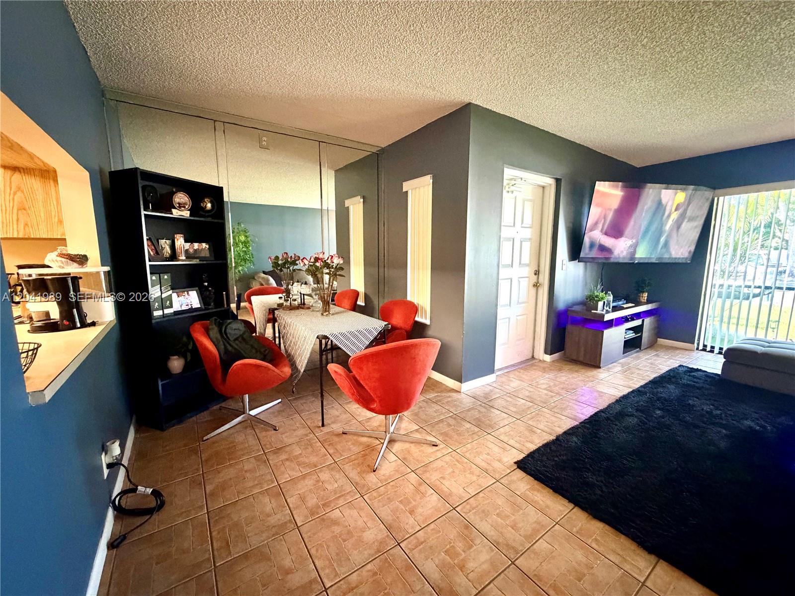 A dining area with red chairs and a mirrored wall sits beside a living room — 1119 Green Pine Blvd # A1, West Palm Beach FL 33409, WEST PALM BEACH, FL