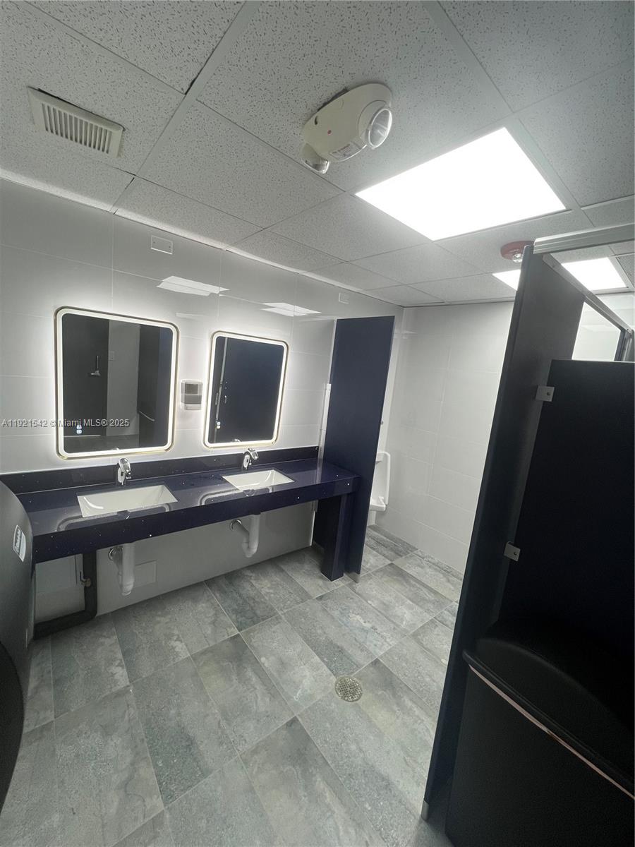 A commercial restroom features two sinks with backlit mirrors, dark countertops, and gray tile flooring — 351 S Cypress Rd, Pompano Beach FL 33060, POMPANO BEACH, FL
