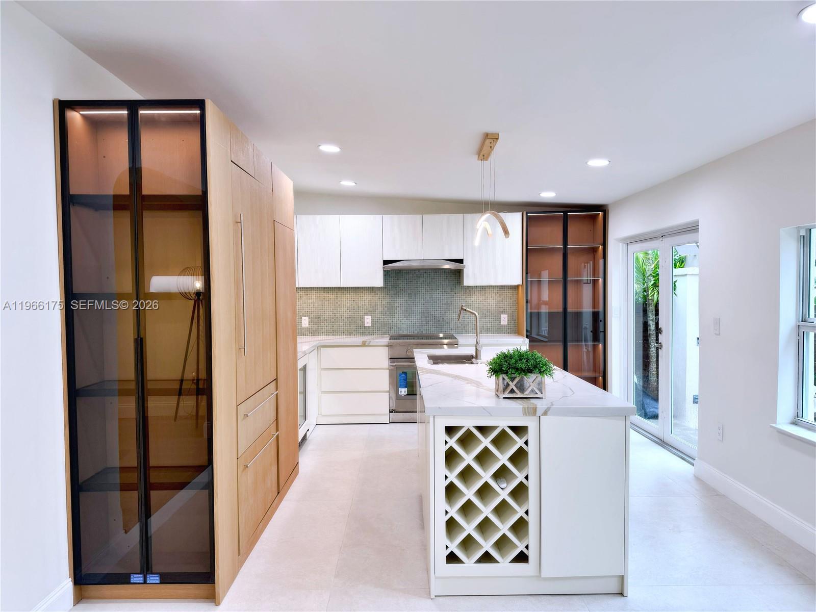A modern kitchen features white cabinets, a marble-topped island with wine storage, and wood cabinetry — 775 NE 76th St, Miami FL 33138, MIAMI, FL