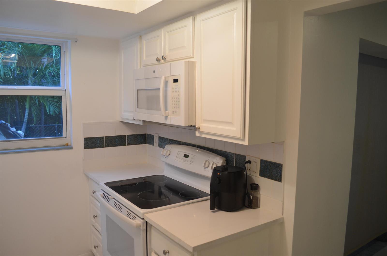 A kitchen features white cabinets, a white electric stove, a microwave, and a window view — 658 NE 6th Court E, Boynton Beach FL 33435, BOYNTON BEACH, FL