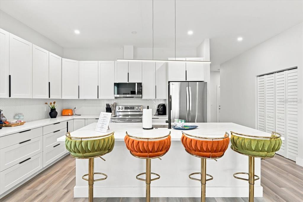 A modern kitchen features white cabinets, stainless steel appliances, and four colorful velvet bar stools — 4390 44TH STREET N, ST PETERSBURG, FL