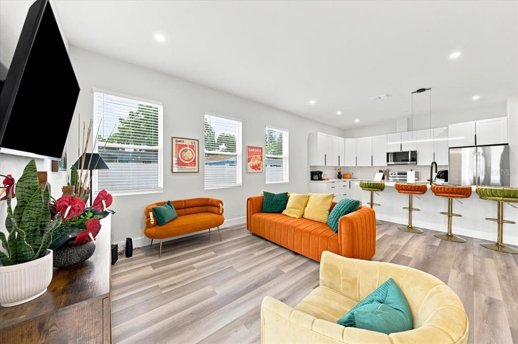 A modern open-concept living room and kitchen with orange sofas and wood-look flooring — 4390 44TH STREET N, ST PETERSBURG, FL