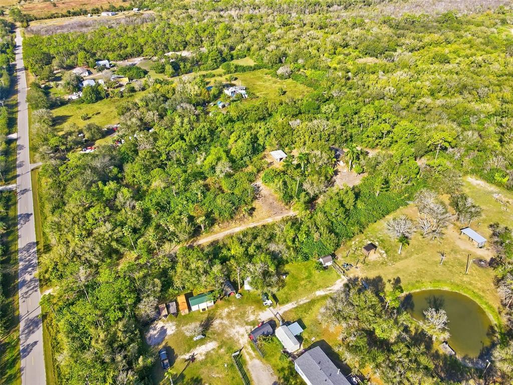 An aerial view shows a rural property with wooded areas, several small buildings, and a pond — 39970 LITTLE FARM ROAD, PUNTA GORDA, FL