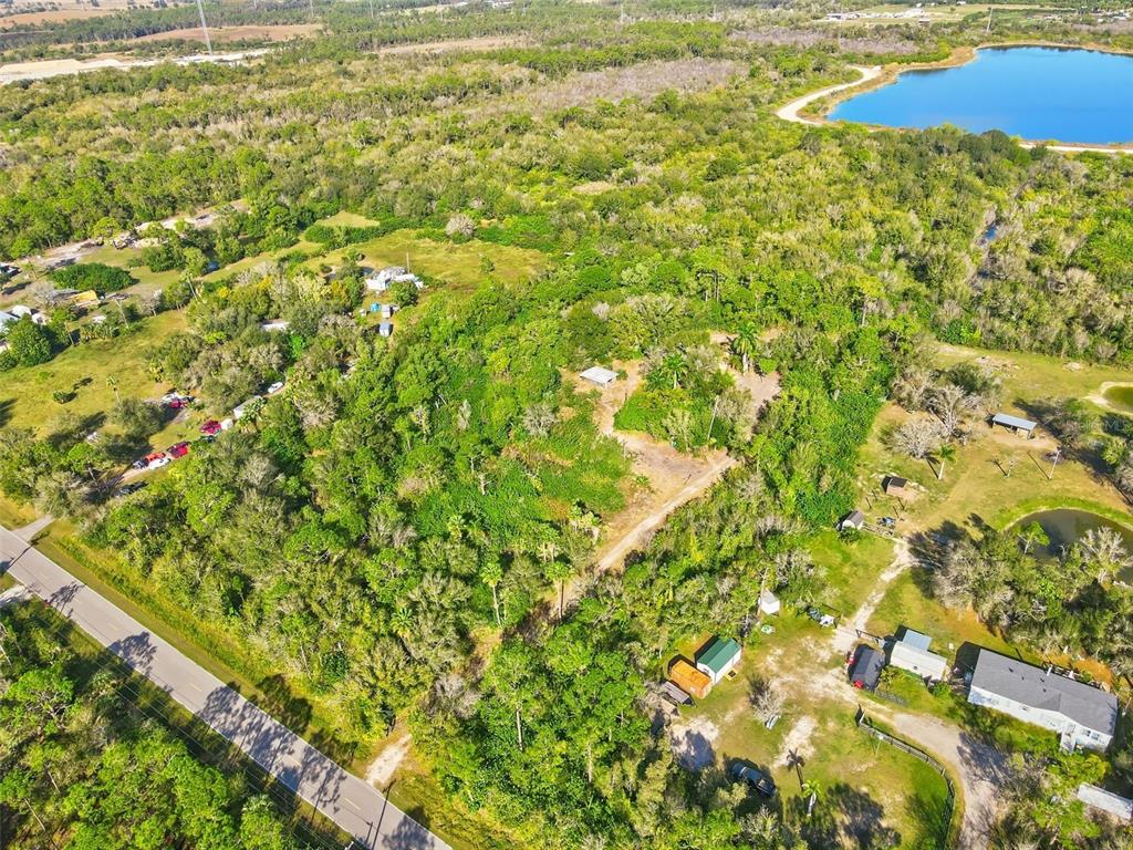 An aerial view shows a wooded lot with several small structures and a nearby lake — 39970 LITTLE FARM ROAD, PUNTA GORDA, FL