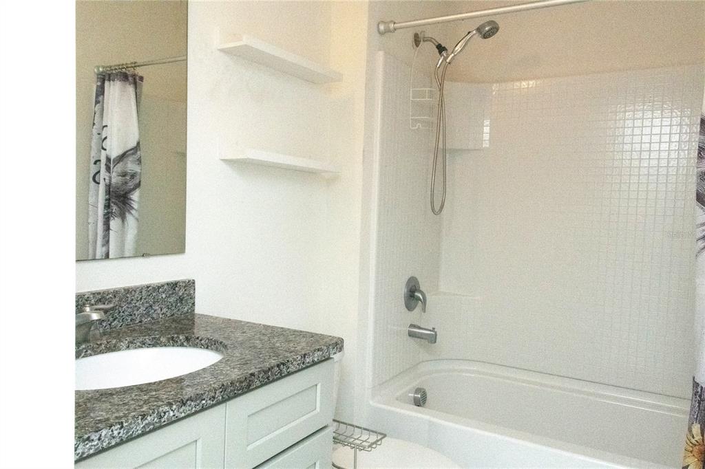 A bathroom features a granite vanity, white cabinets, floating shelves, and a shower-tub combination — 3940 SILVERSTREAM TERRACE, SANFORD, FL