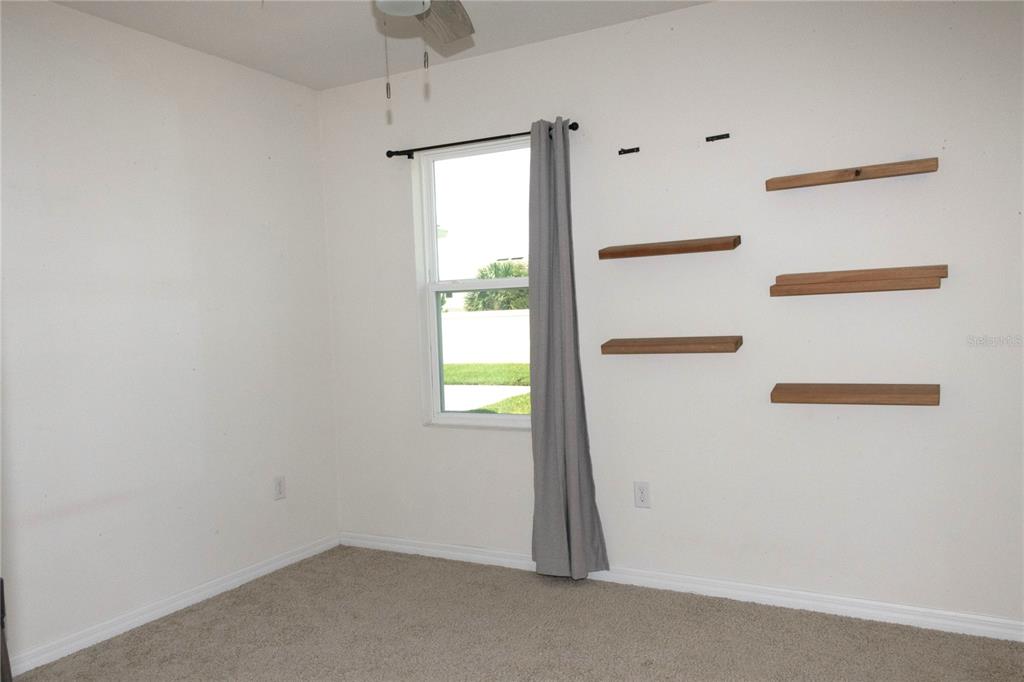 An empty bedroom features beige carpet, white walls, a single window, and several wall-mounted shelves — 3940 SILVERSTREAM TERRACE, SANFORD, FL
