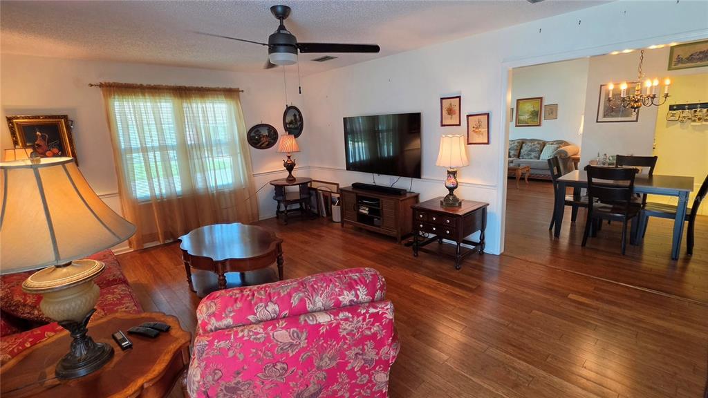 A living room with hardwood floors, a floral sofa, a television, and an adjacent dining area — 4 BIRDIE DRIVE, NEW SMYRNA BEACH, FL