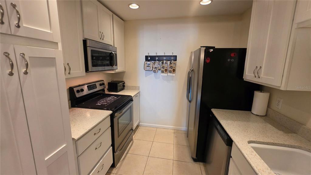 A galley kitchen features white cabinets, stainless steel appliances, and light-colored countertops — 4 BIRDIE DRIVE, NEW SMYRNA BEACH, FL