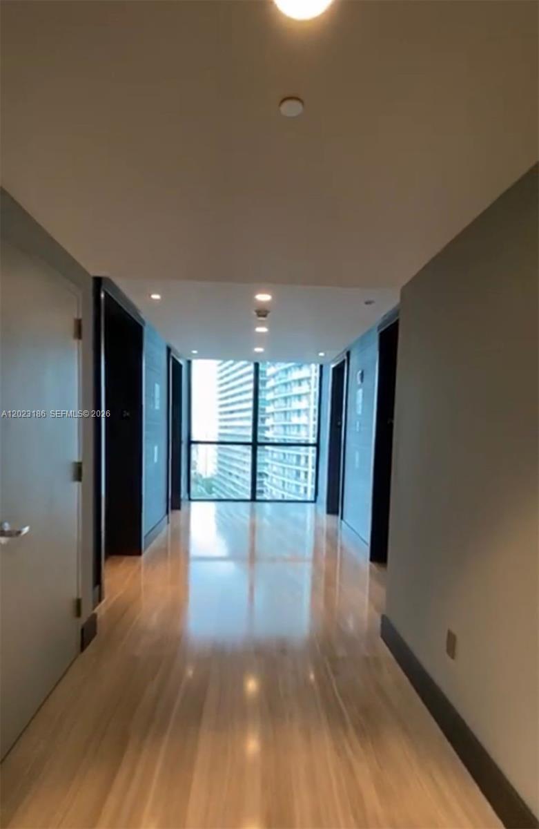 A hallway with light wood flooring leads to a floor-to-ceiling window overlooking city buildings — 1080 Brickell Ave # 2405, Miami FL 33131, MIAMI, FL