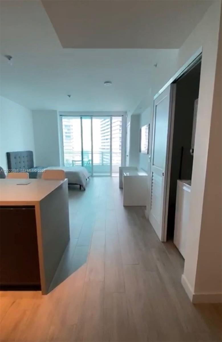 A modern studio apartment features light wood flooring, a kitchen island, and a balcony entrance — 1080 Brickell Ave # 2405, Miami FL 33131, MIAMI, FL