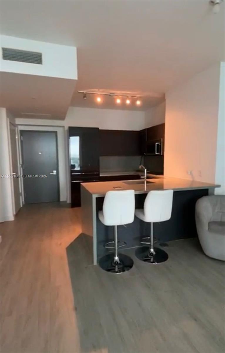 A modern kitchen features dark cabinetry, a central island with bar stools, and light flooring — 1080 Brickell Ave # 2405, Miami FL 33131, MIAMI, FL