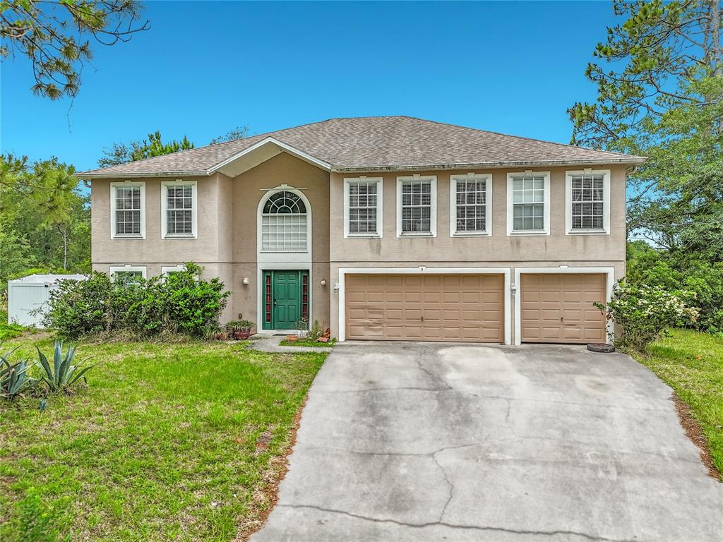 A two-story house with a tan stucco exterior, a three-car garage, and a green door — 9 BURNE PLACE, PALM COAST, FL