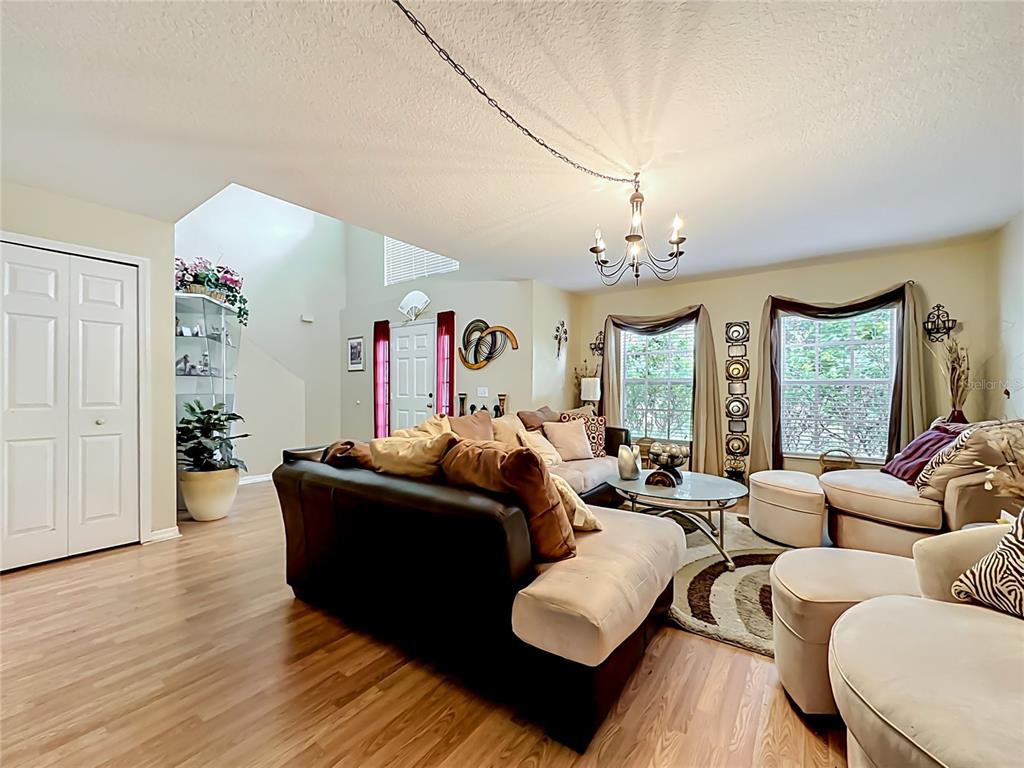 A living room features a dark sofa, light-colored armchairs, a chandelier, and wood-look flooring — 9 BURNE PLACE, PALM COAST, FL