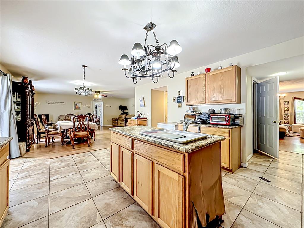 A kitchen with a central island, wooden cabinets, and tile flooring opens to a dining area — 9 BURNE PLACE, PALM COAST, FL